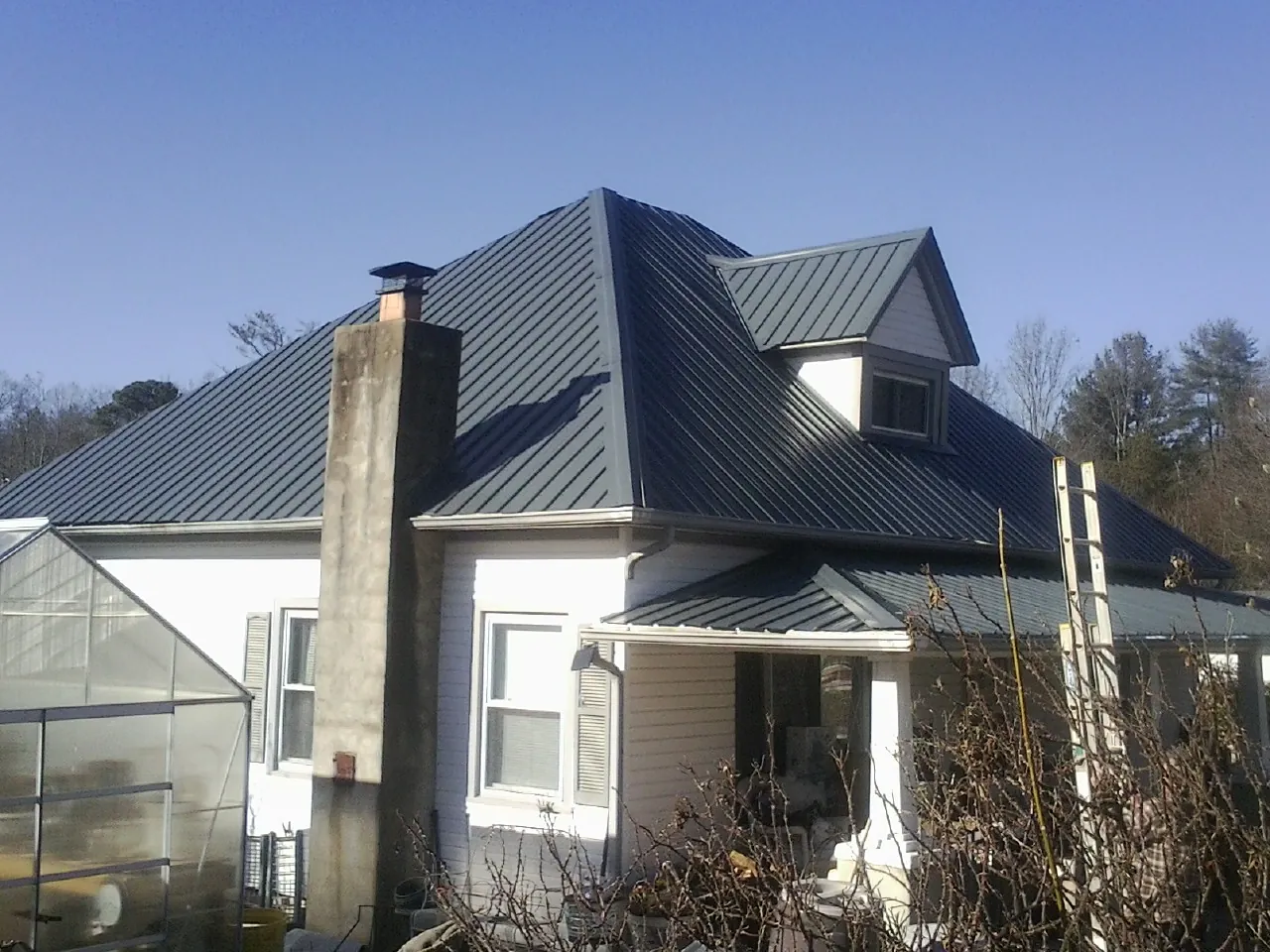 Dark blue standing seam metal roof on a white farmhouse with dormer — Slate & Tile Roof Repair by Roofing Brothers in Monterey Park