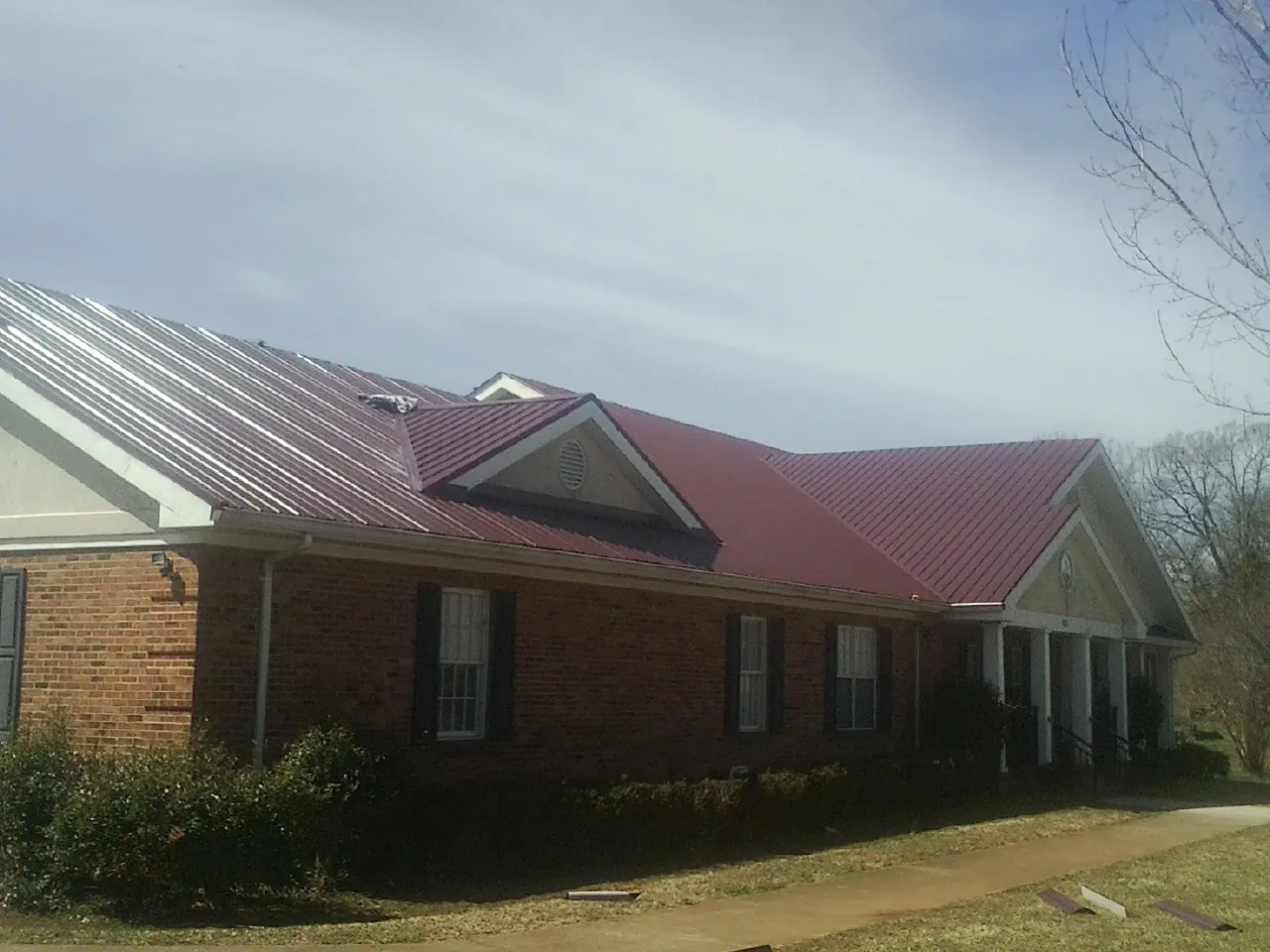 Red metal roof with gabled entries on a long brick building, from a Hail Damage Roof Repair job in Monterey Park
