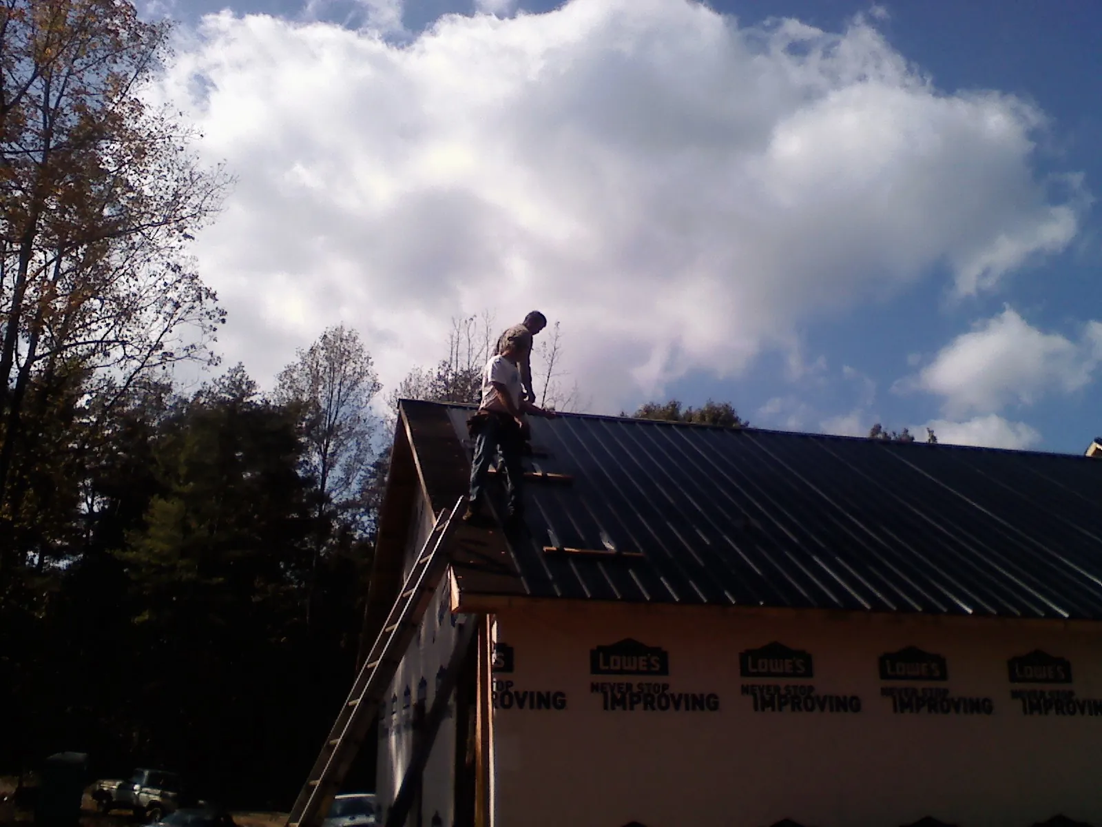 Roofer fastening dark metal panels high against a cloudy sky, from a Roof Inspection job in Monterey Park