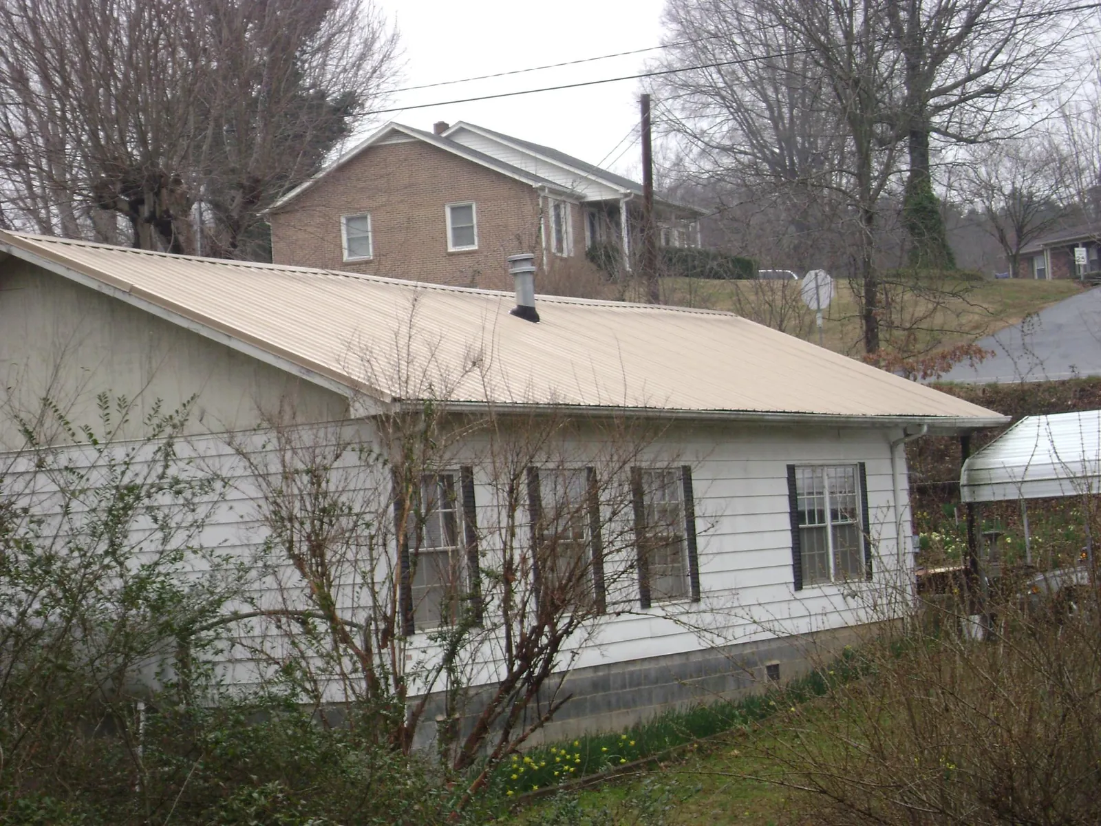 Tan metal roof on a white sided house set into a hillside — Commercial Roofing by Roofing Brothers in Monterey Park
